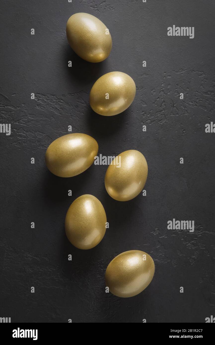 Chicken colored golden eggs on black. Easter creative dark concept. View from above. Minimal composition. Stock Photo