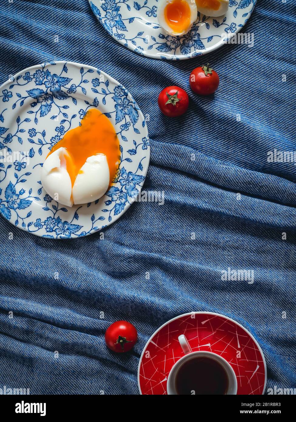 Soft boiled eggs on blue patterned plates and red coffee cup on a blue linen Stock Photo