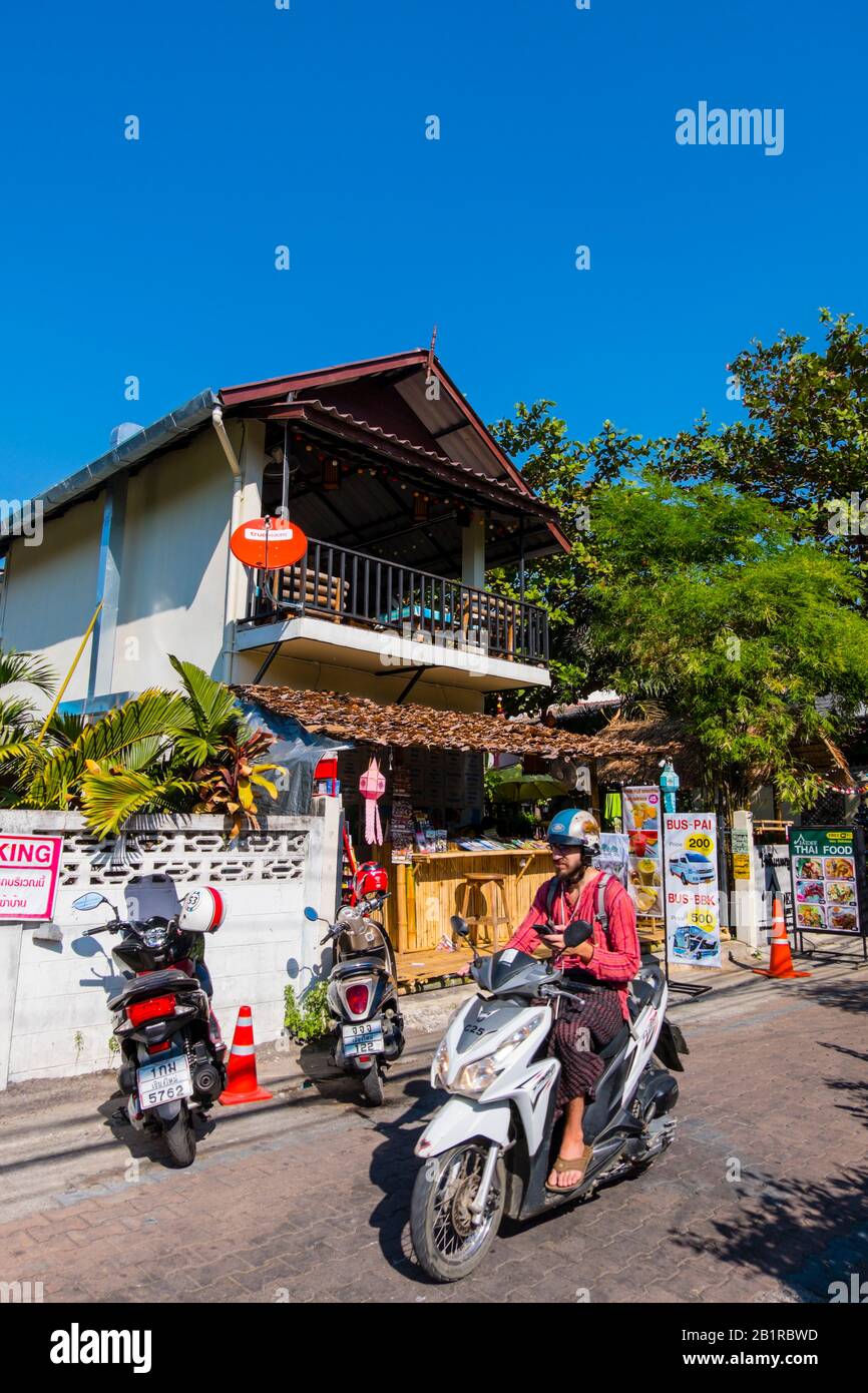 Tourist man riding a scooter with a smart phone in hand, old town, Chiang Mai, Thailand Stock Photo