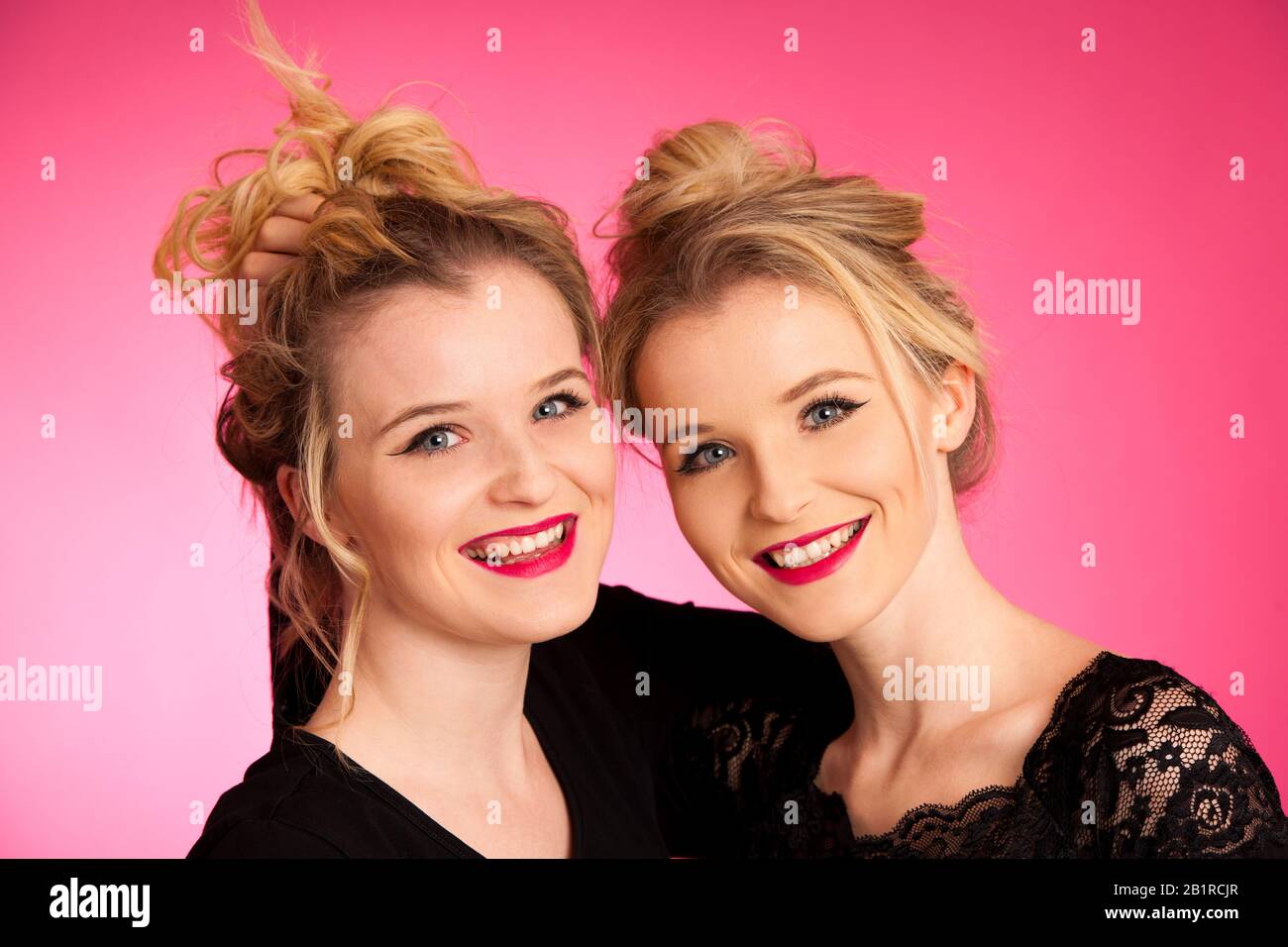 Portrait of twin sisters over pink background Stock Photo
