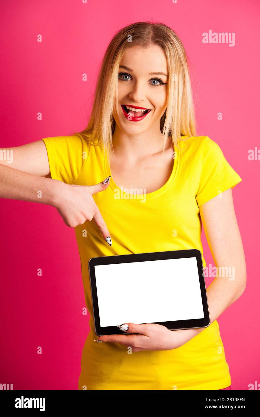 Beautiful blonde teenage woman pounting in blank tablet as advertisement over pink background Stock Photo