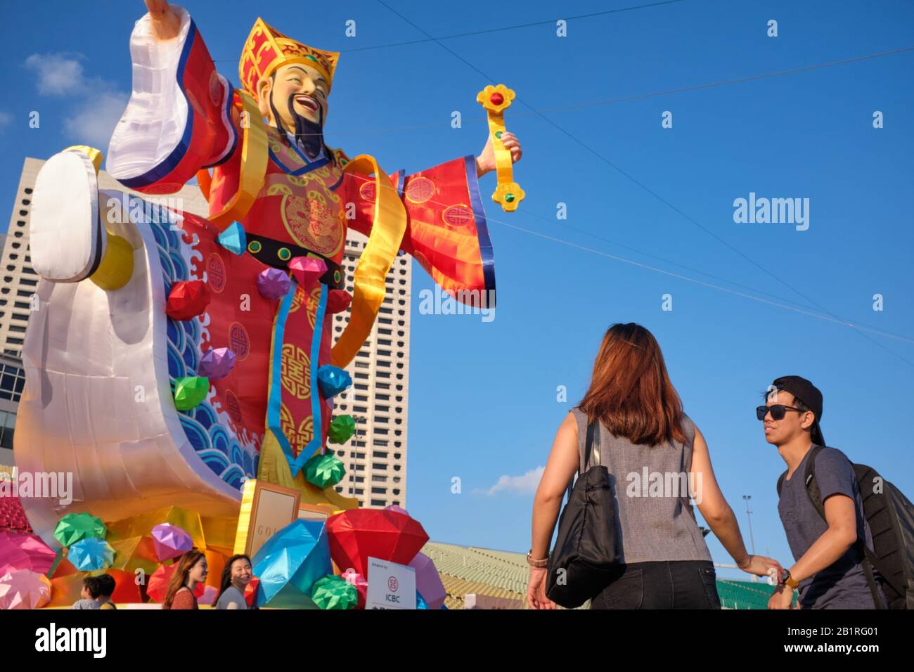 A tourist couple at thestatue of the Chinese God of Good Fortune / Wealth, erected for Chinese New Year celebrations; Esplanade, Marina Bay, Singapore Stock Photo