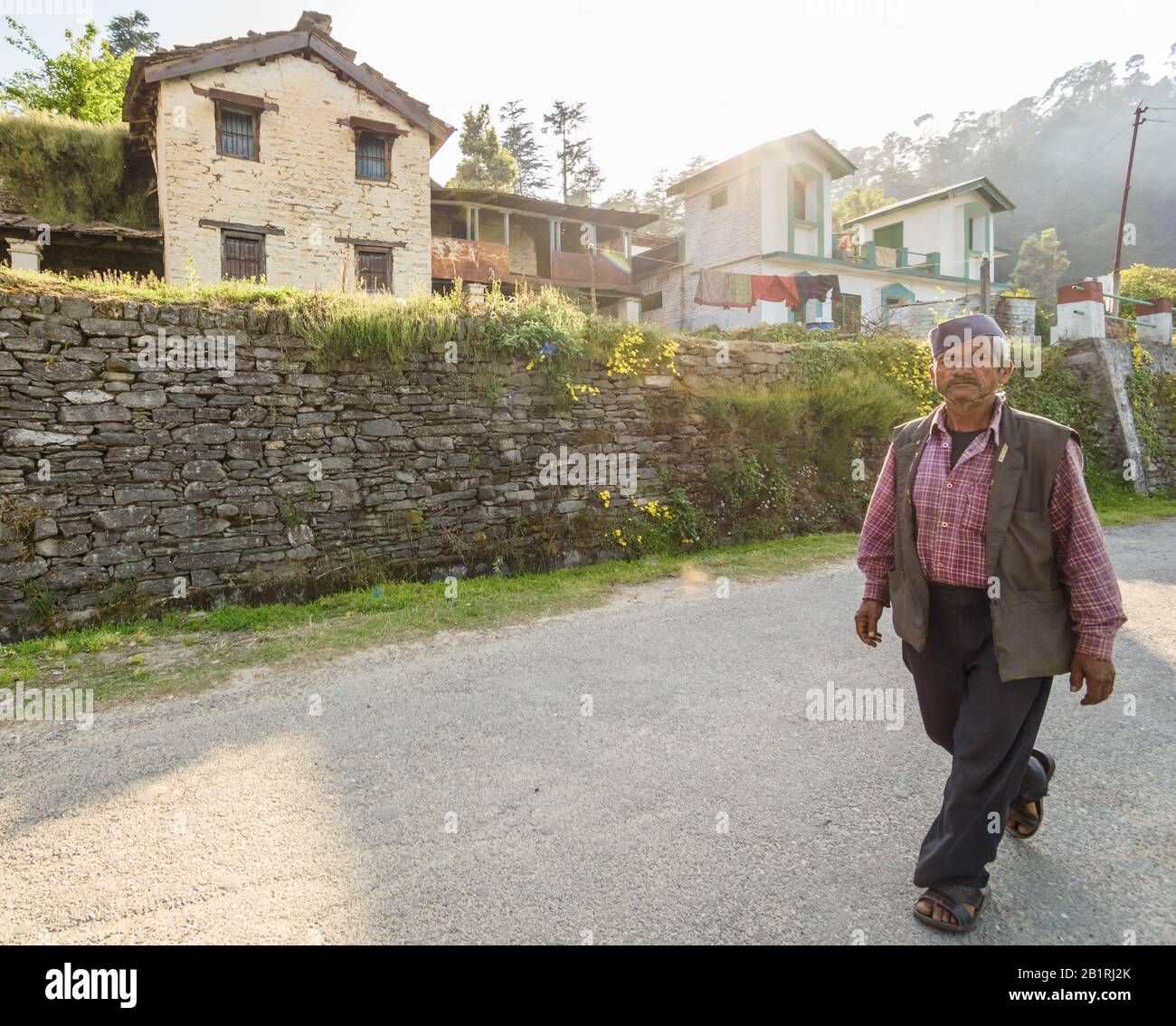 Kausani, Uttarakhand/India - April 3 2019: Wide angle shot of a man walking past a traditional Kumaoni wood and stone house fenced by a stone wall. Stock Photo