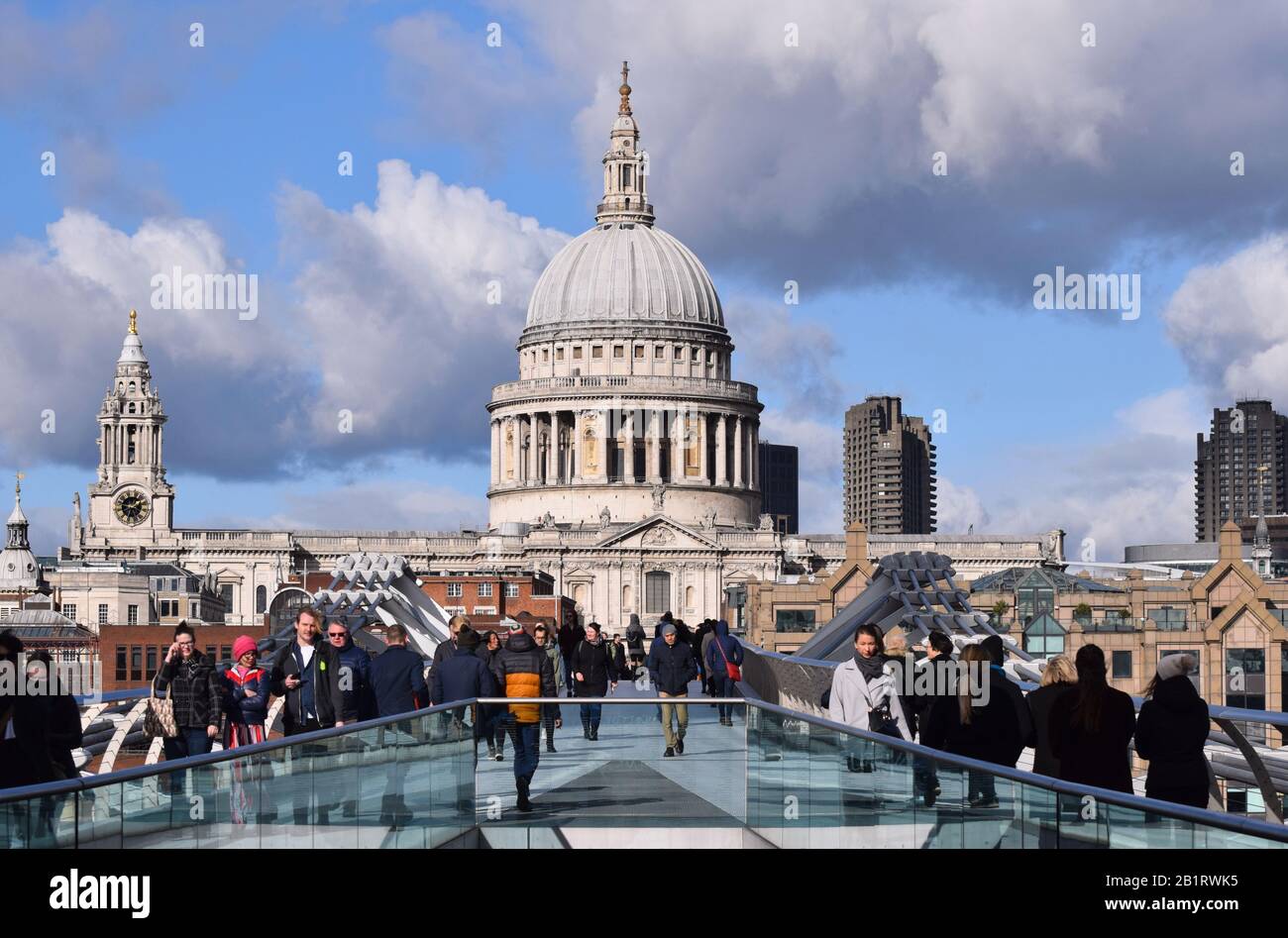 The view along the Millennium Bridge London to the dome of St Pauls Cathedral with an interesting sky of blue sky and clouds with people on the bridge Stock Photo