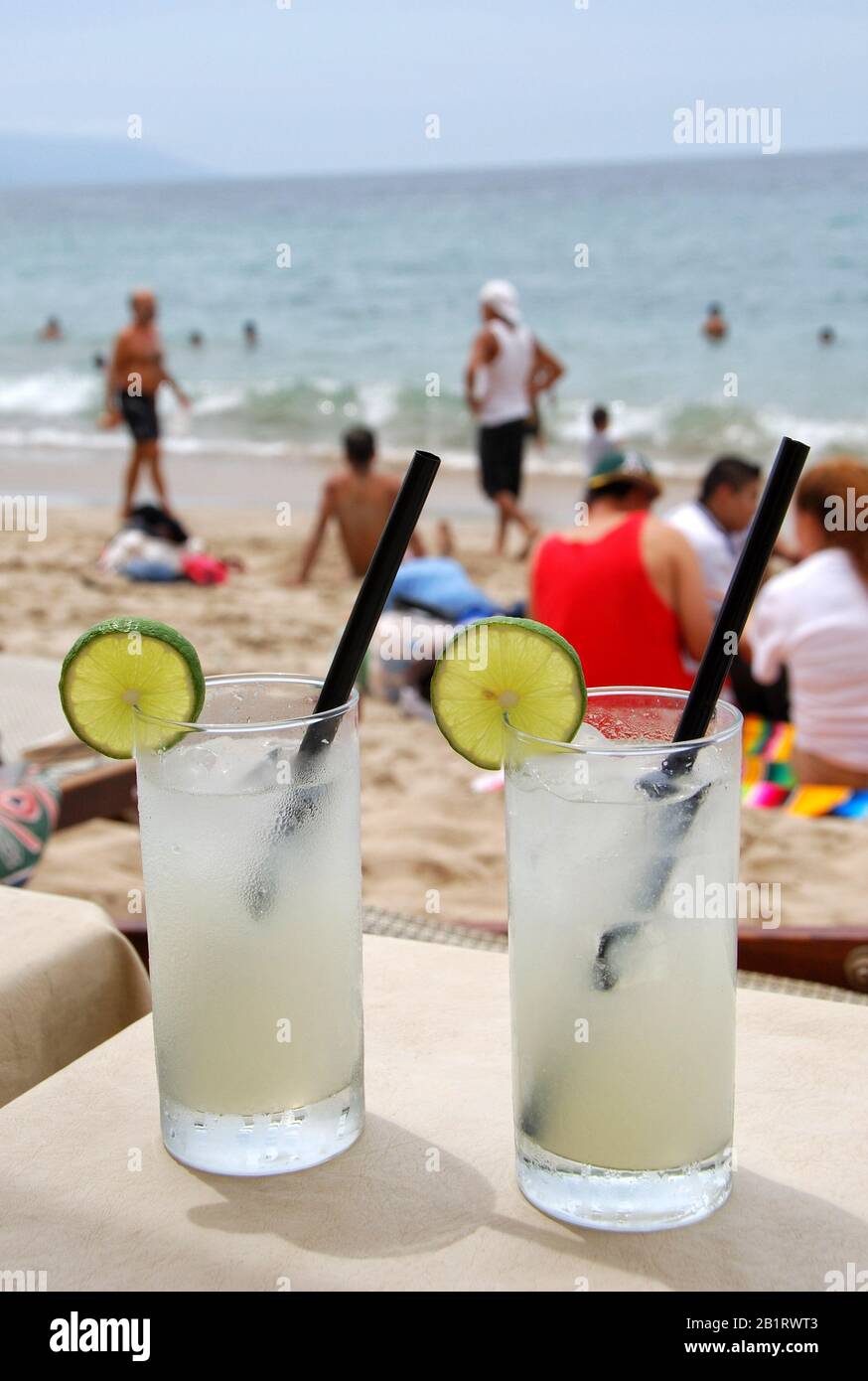 Two frozen Margarita cocktails at beach bar. People walking and sitting