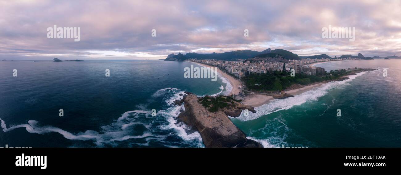 Swirling wave pattern at Arpoador rock in Rio de Janeiro, Brazil, with Ipanema beach and wider cityscape in the background against a colourful sky Stock Photo