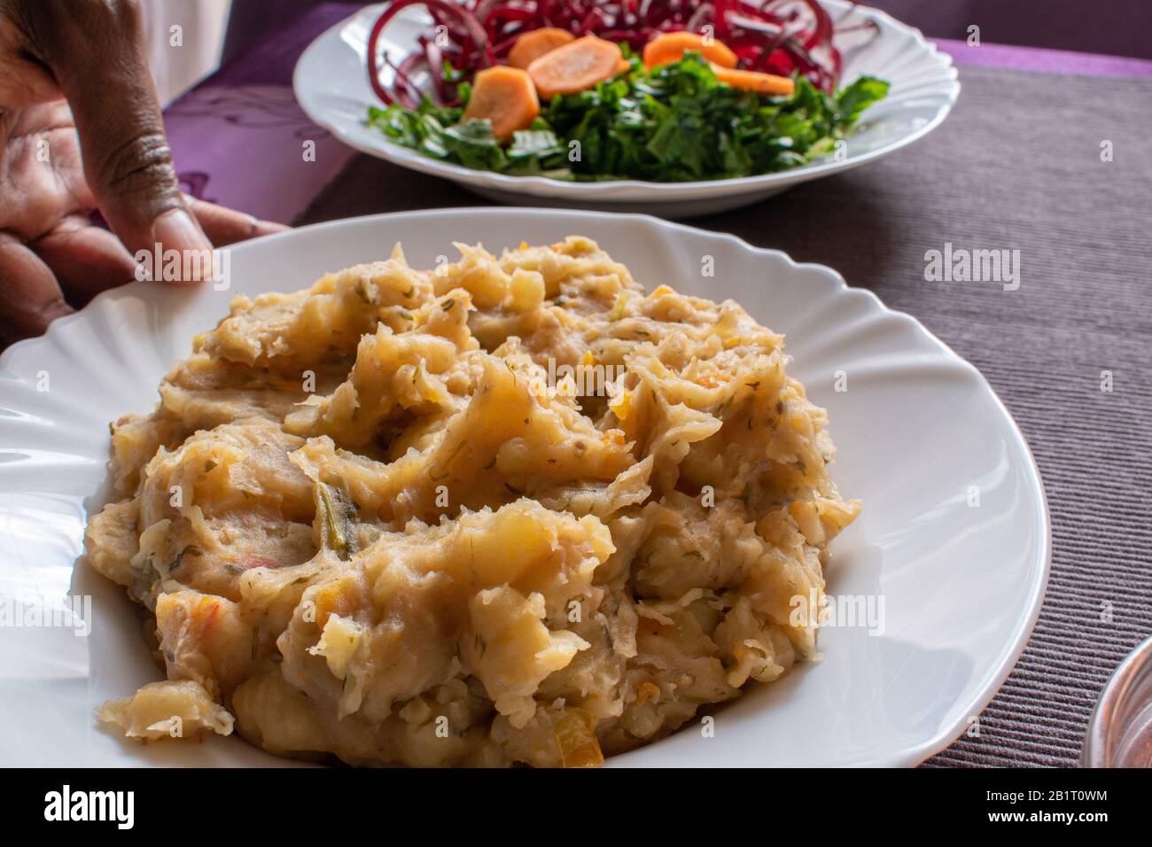 a plate of matoke being held by a hand on a table Stock Photo