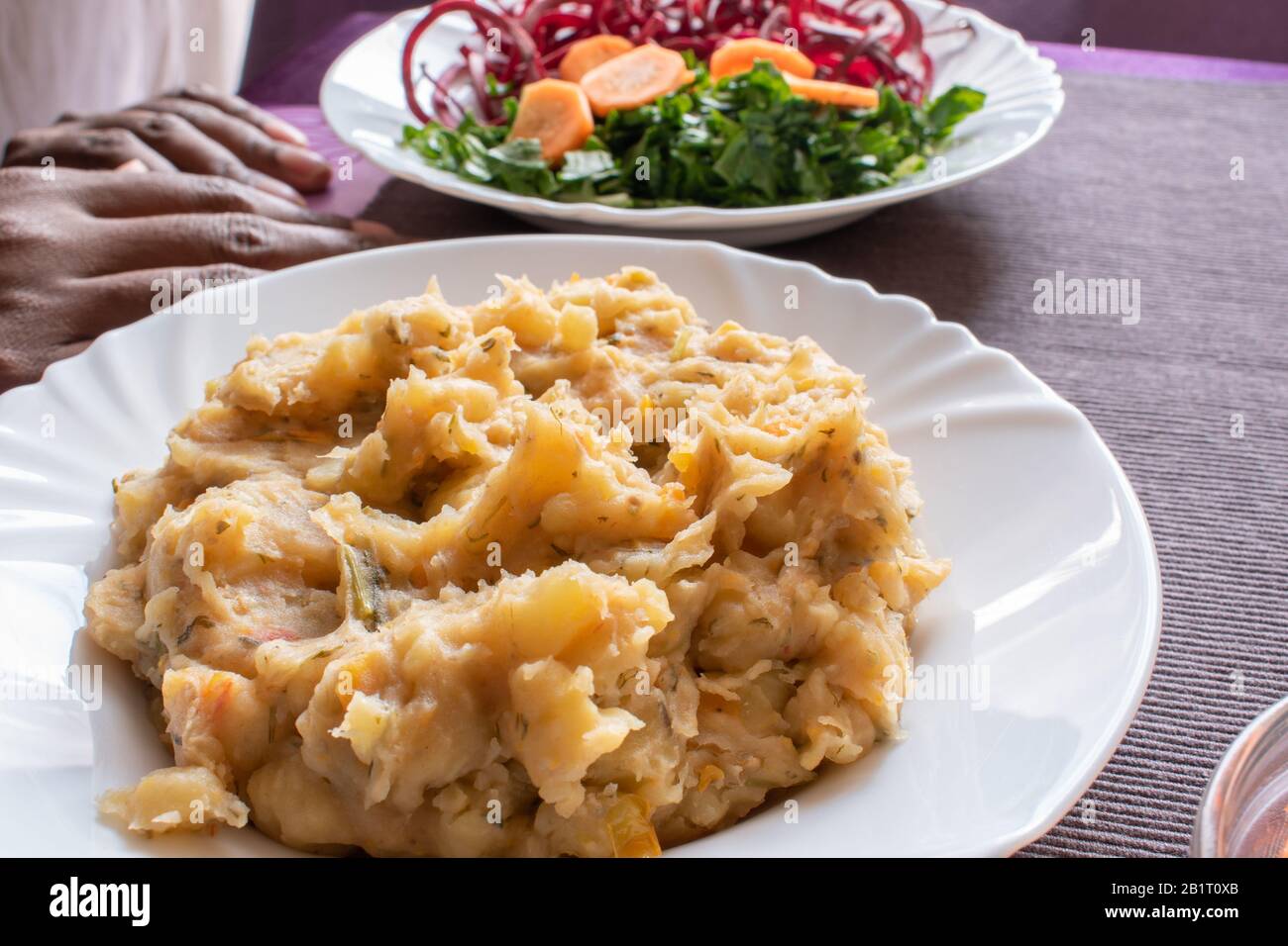 a plate of matoke next to vegetable . matoke is traditional food made using unripe banana. Stock Photo