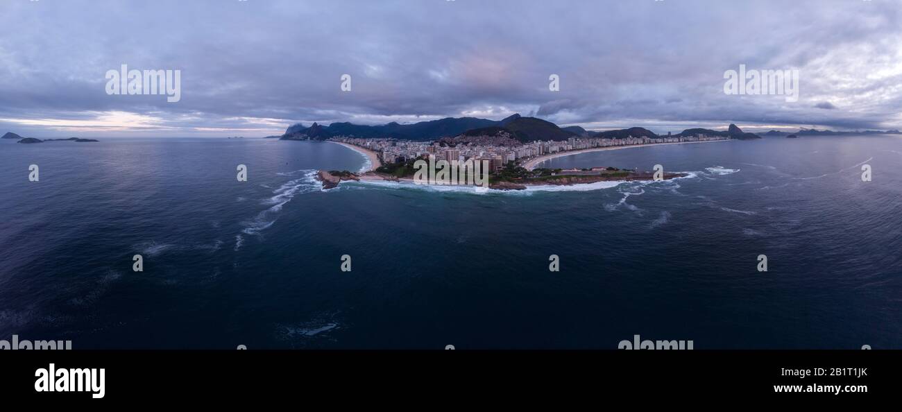Copacabana fort and Arpoador rock in the foreground with wider Rio de Janeiro cityscape in the background against an overcast sky at sunrise Stock Photo