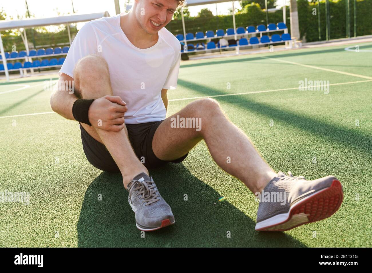 Image of tense man in sportswear having trauma and suffering from pain while sitting on playground outdoors Stock Photo