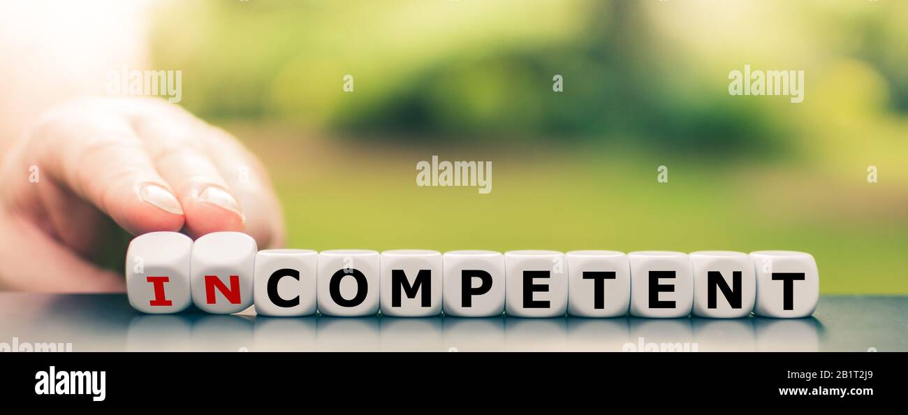Hand turns dice and changes the word 'incompetent' to 'competent'. Stock Photo