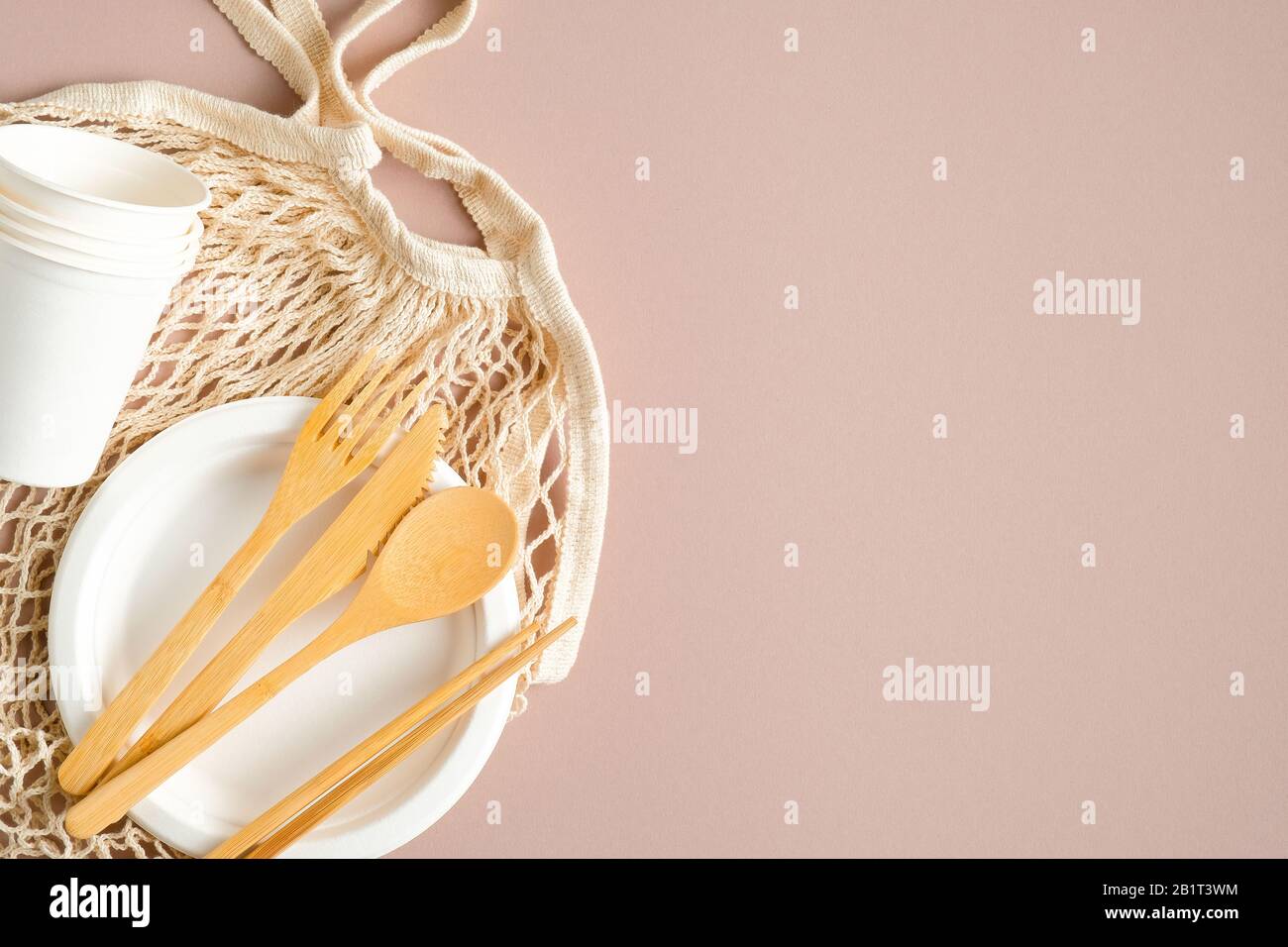 Reusable grocery mesh bag, wooden cutlery set, paper cups and plate on ...