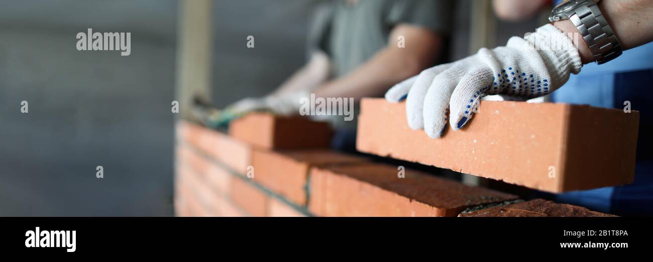 Two workers making red brick wall at construction site Stock Photo