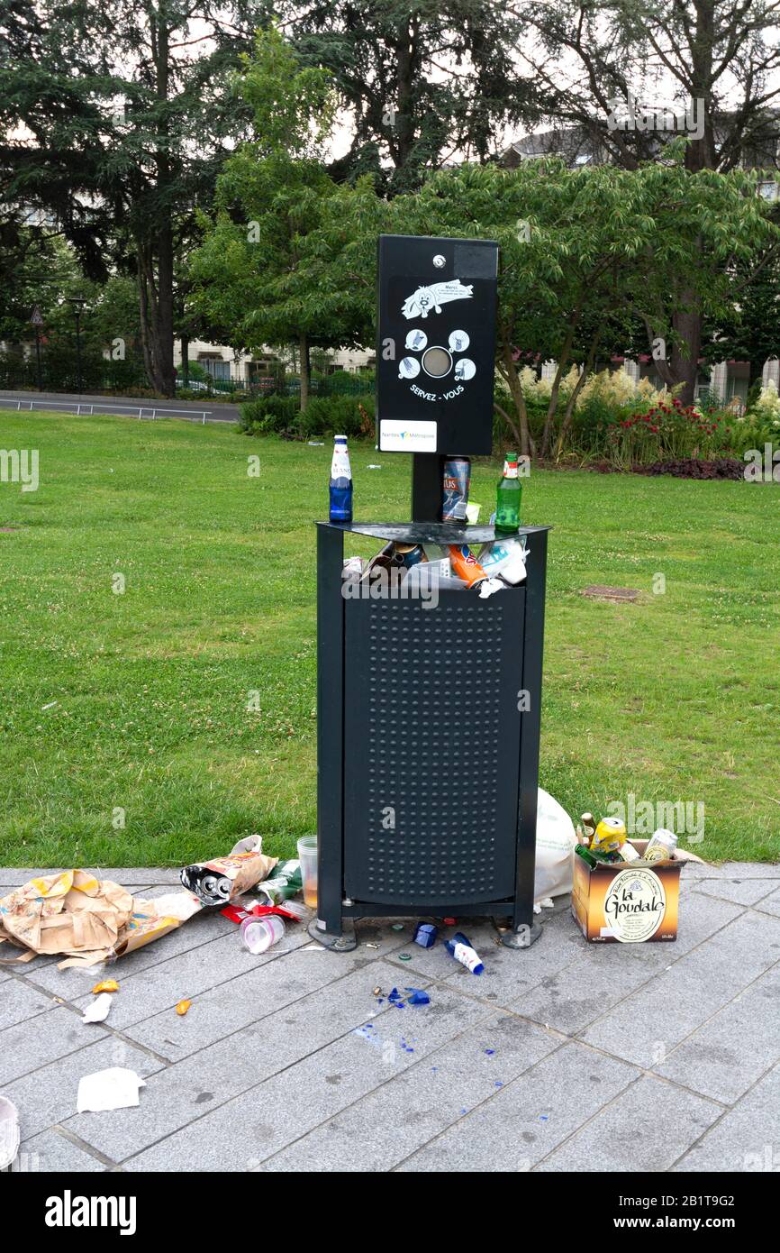 Full litter bin overflowing with rubbish in a public park after a party. France Stock Photo