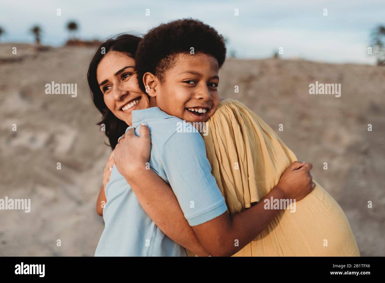 Close up of young mother and happy son embracing on beach at sunset Stock Photo