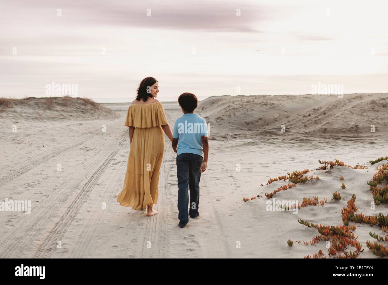 young-mother-and-school-aged-son-walking-at-beach-against-cloudy-sky-2B1TFY4.jpg