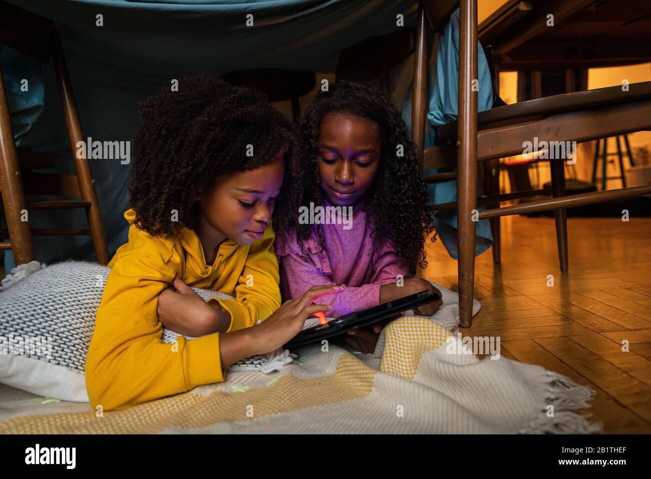 Sisters using digital tablet while lying on blanket at home Stock Photo