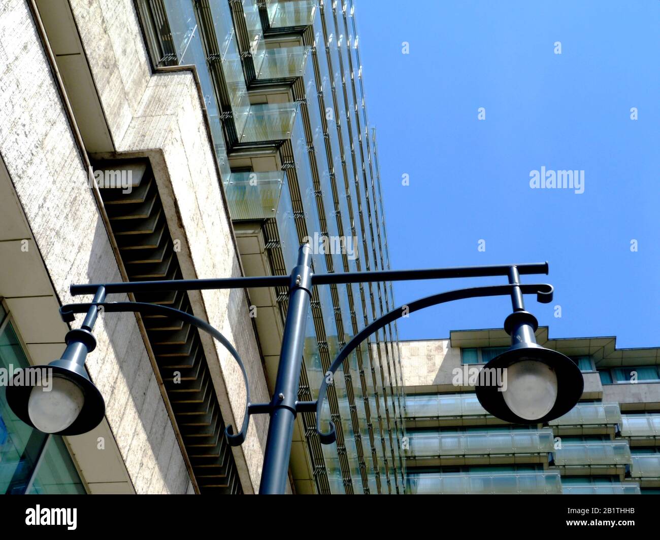 view of vintage style street lamps on skinny tall steel posts and large glass lens covers and stylish glass exterior corridors of hotel building Stock Photo