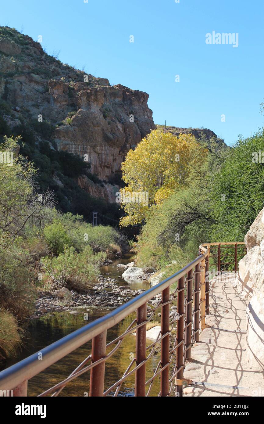 A metal railing along a trail carved into a mountainside along a creek ...