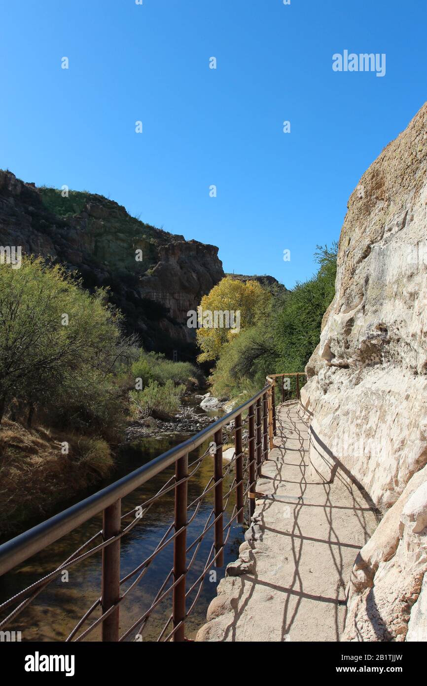 A metal railing along a trail carved into a mountainside along a creek ...