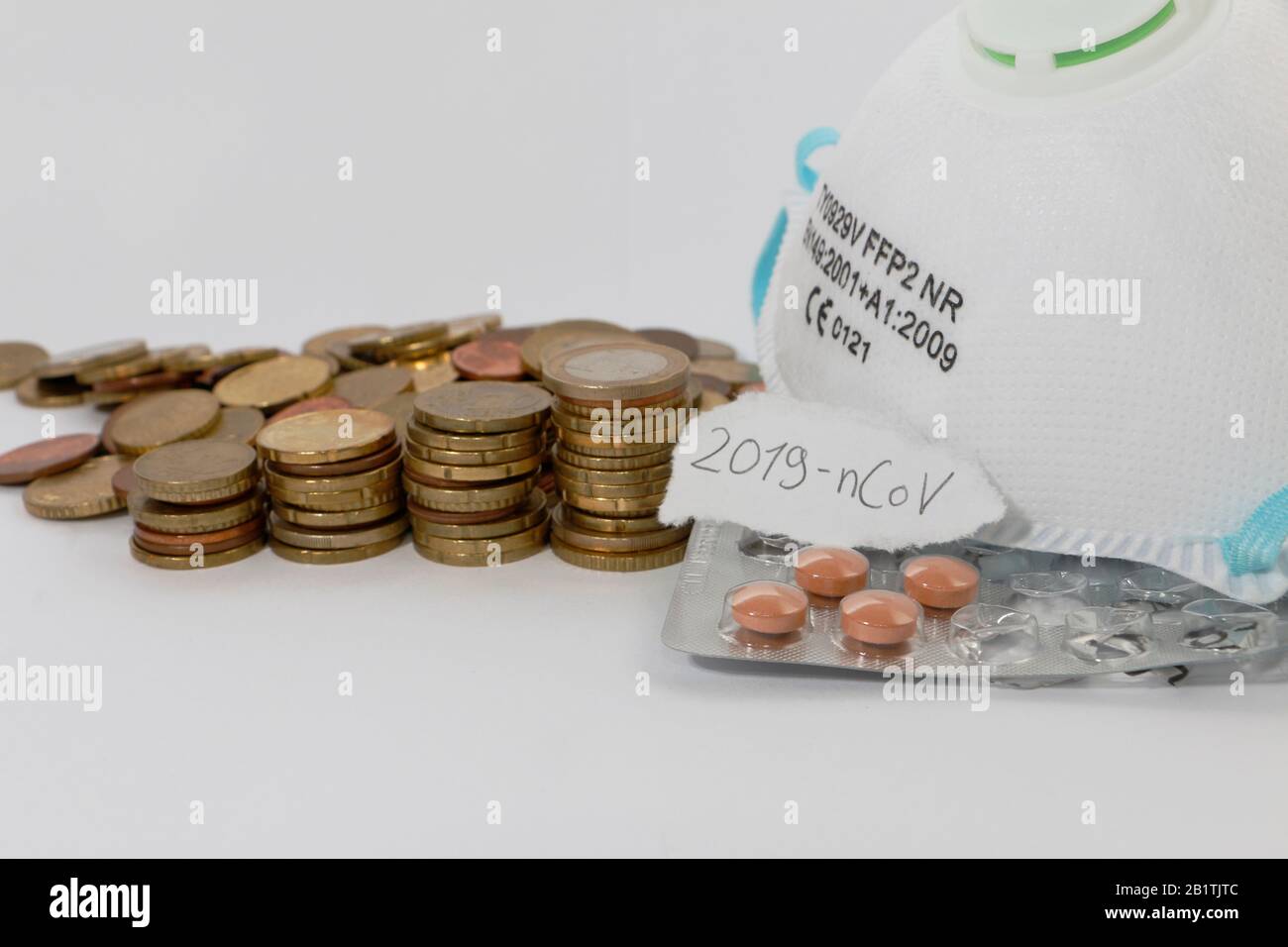 FREIBURG, GERMANY - FEB 24, 2020: A medical mask, coins and medication representing the increasing costs caused by the new corona virus / 2019-nCov. T Stock Photo