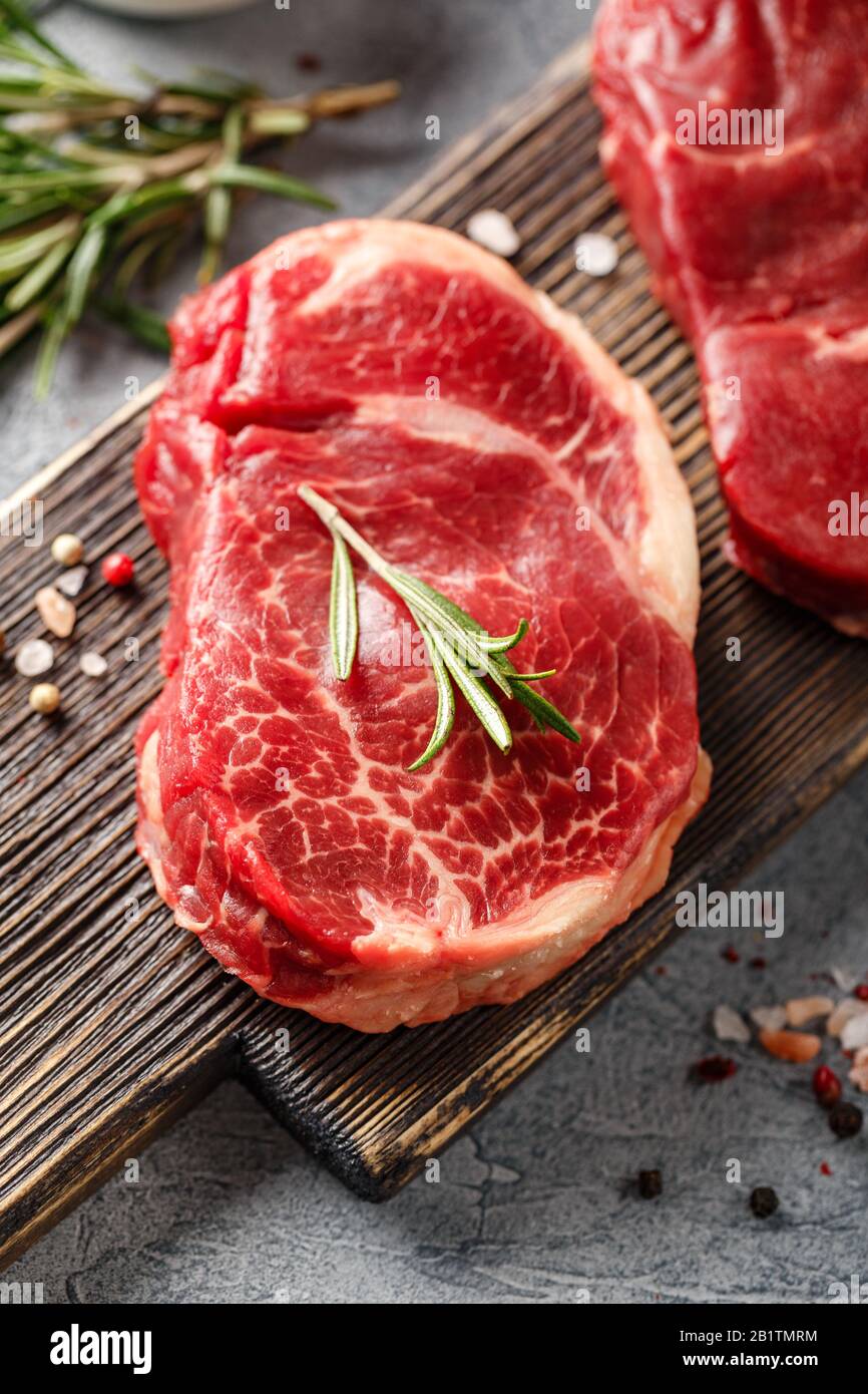 Three pieces of traditional thin steak cut from the tenderloin on wooden cutting board with olive oil, salt, rosemary and pepper. Raw Black Angus Prim Stock Photo