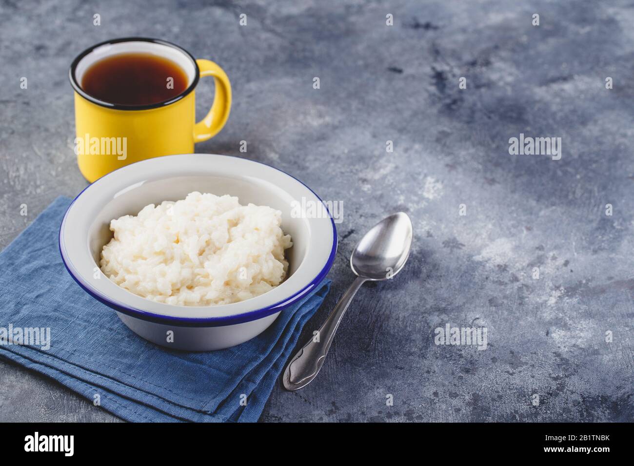 Milk rice porridge, creamy rice pudding or french riz au lait in a metal bowl and enamel mug with tea. Place for text Stock Photo