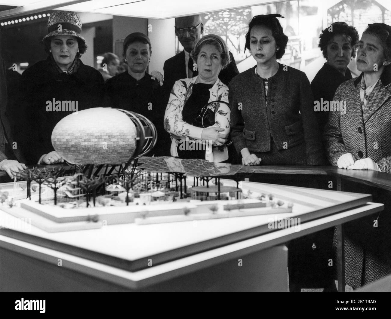 Women gathered around an architectural design model of the IBM pavilion with man-made steel trees and Ovoid Theater, designed by Charles Eames and Eero Saarinen for the 1964 New York World's Fair. The pavilion model was on display at the IBM Business Show in Manhattan at the New York Coliseum, coinciding with the April 30, 1963 IBM Stockholder's Annual Meeting. Stock Photo