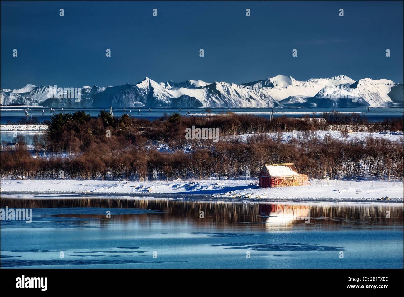 Red barn reflecting in water in Norway; winter landscape with mountains in the background Stock Photo