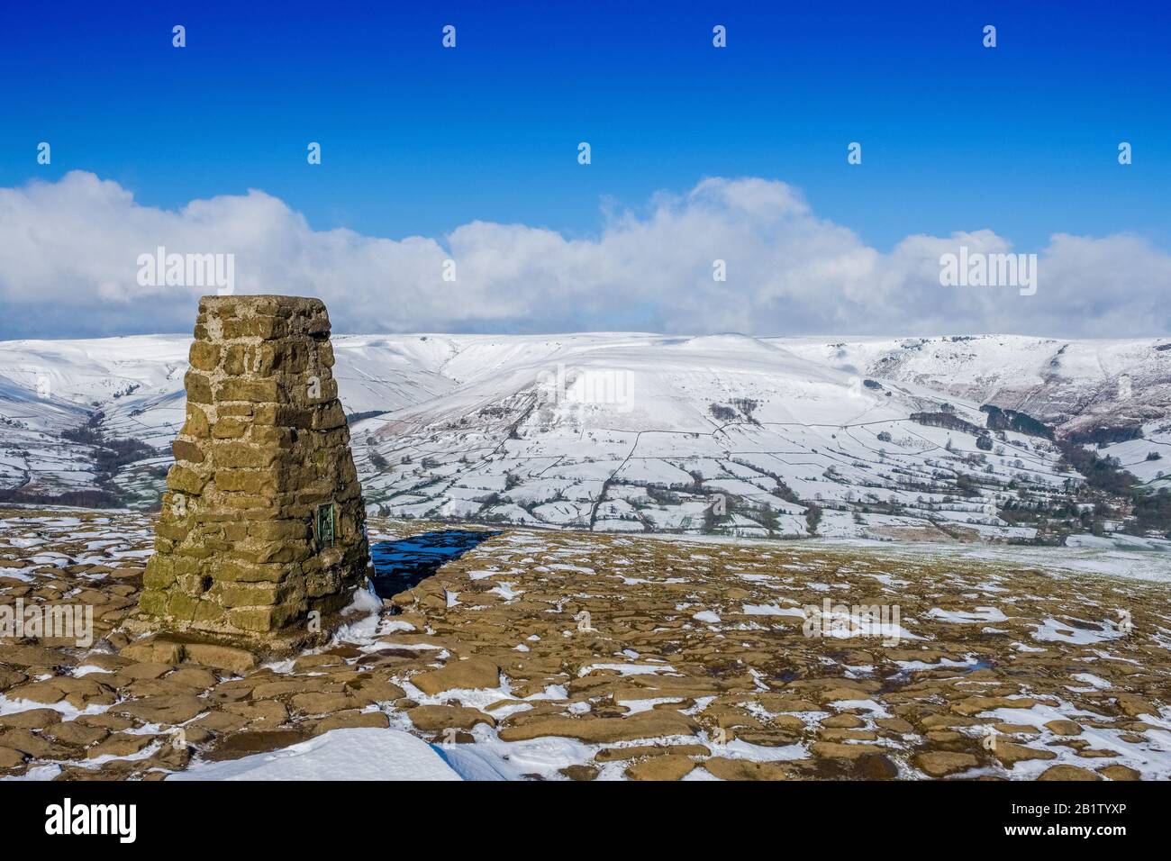 The summit trig point of Mam Tor in the Peak District National Park, with Edale & Kinder Scout in the distance Stock Photo
