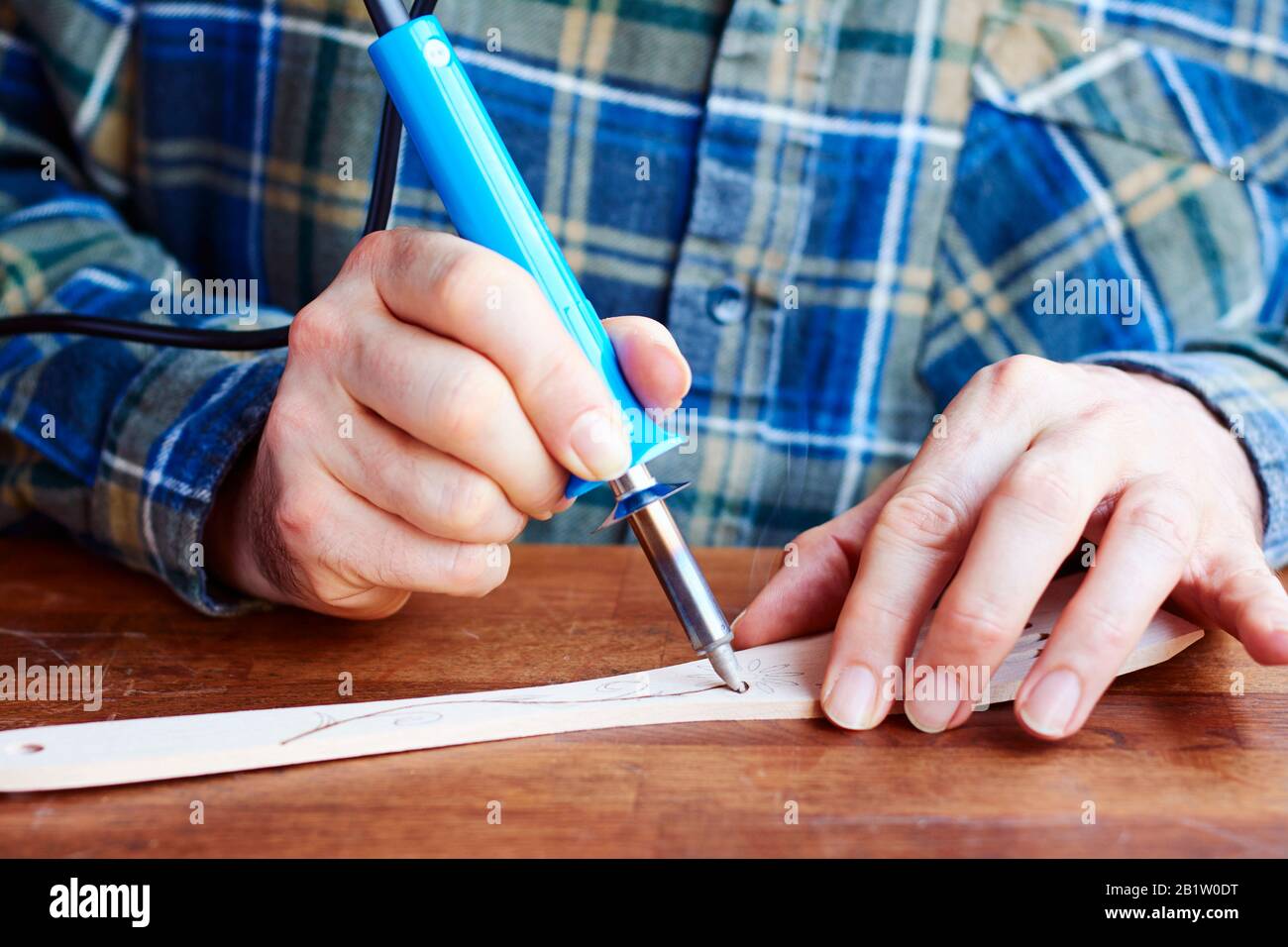 Man decorating a wooden slotted turner with a flower design using a