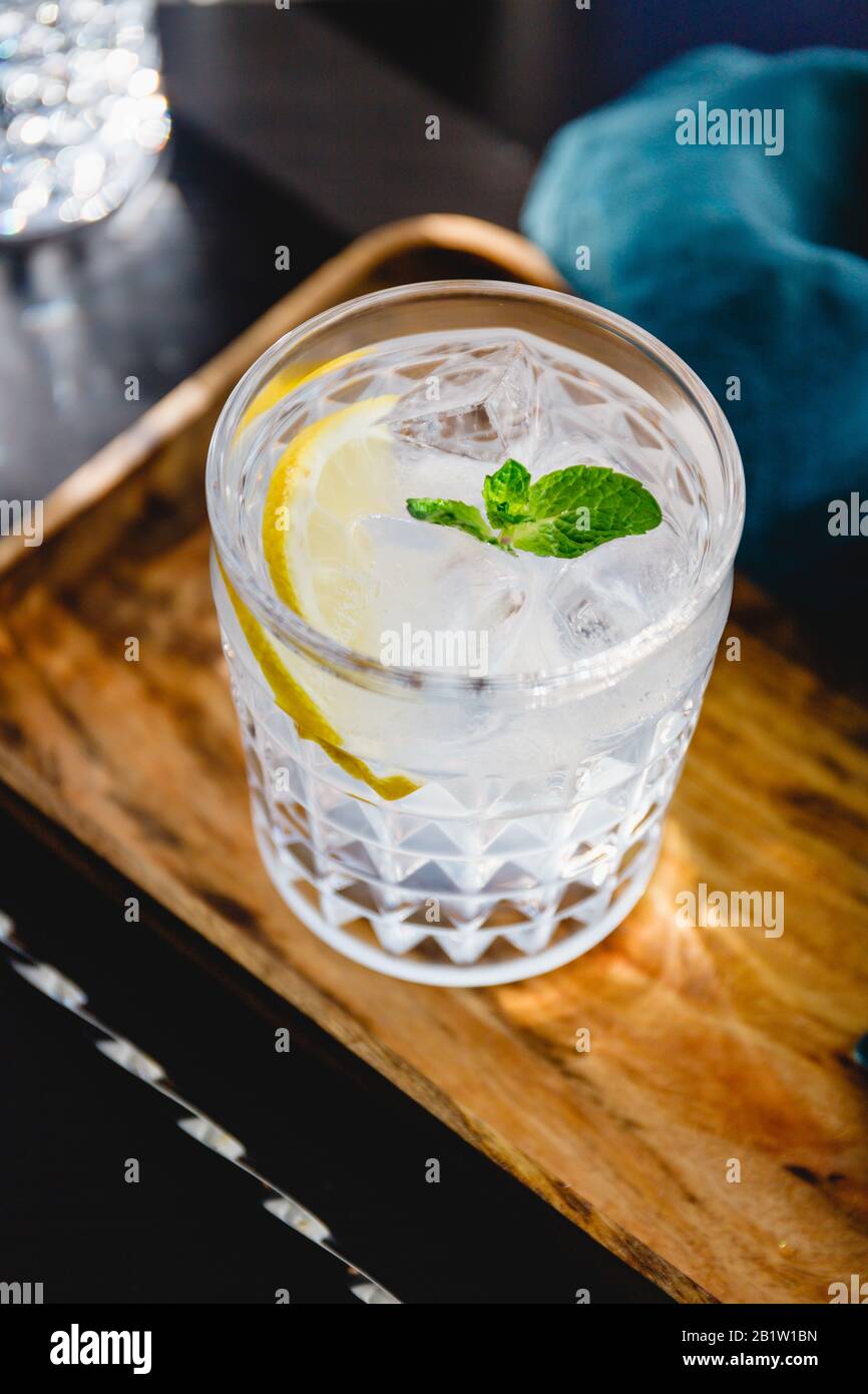 Refreshing cold summer cocktail with soda water, lemon and ice cubes on a wooden tray. Stock Photo