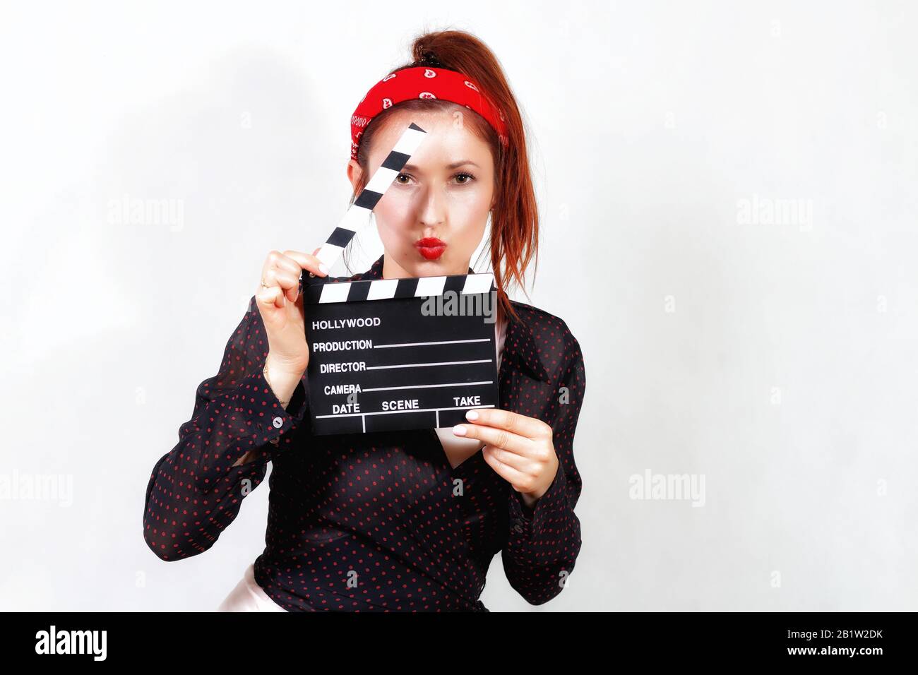 Young redhead pin up woman in bandana and black shirt with red lips kissing through movie clapper Stock Photo