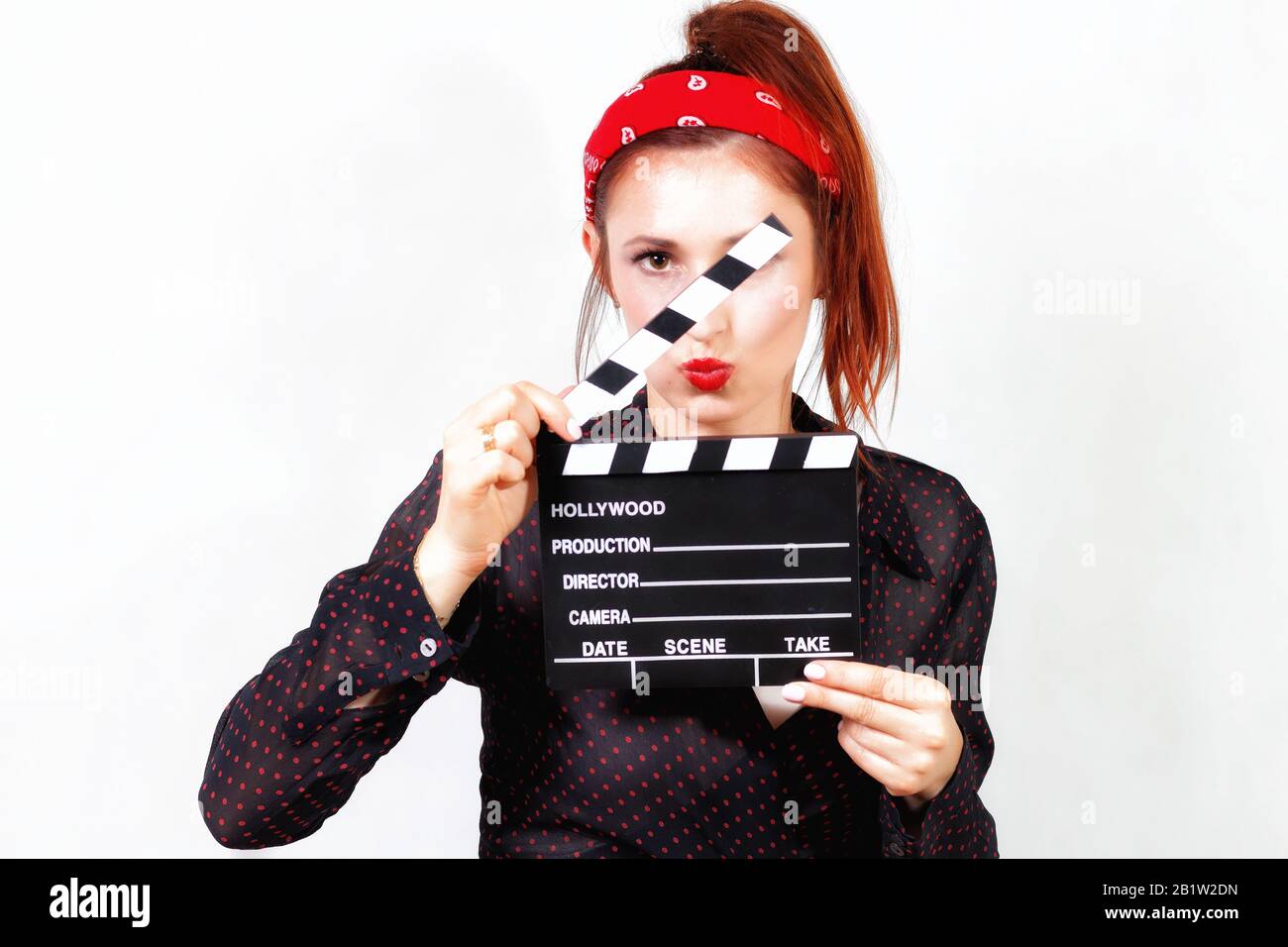 Young redhead pin up woman in bandana with red lips kissing through movie clapper Stock Photo