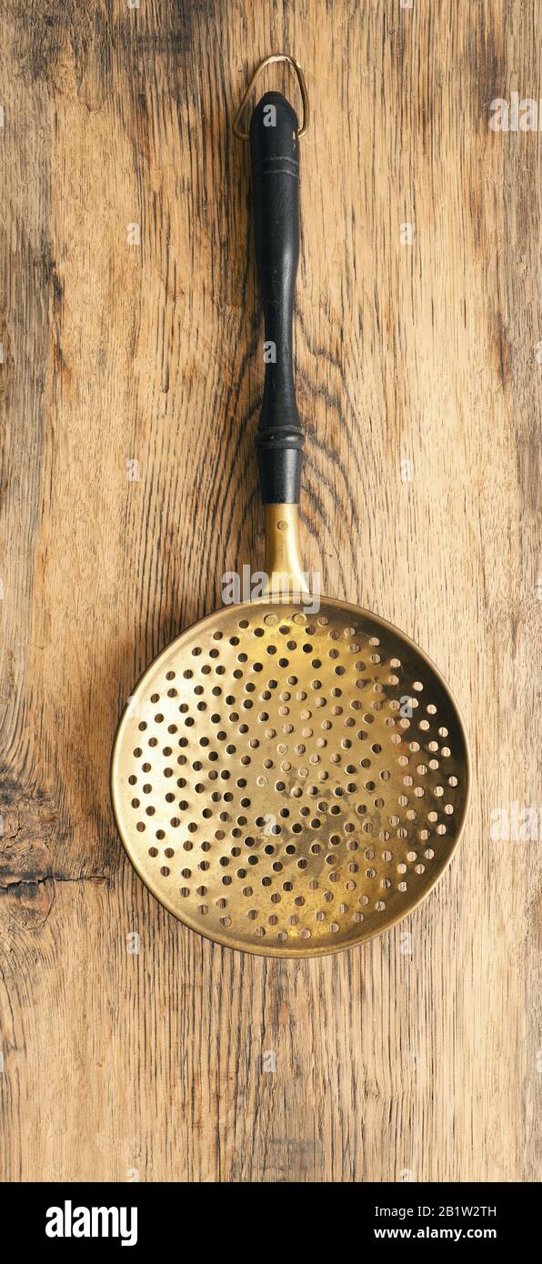 Old used skimmer on a rustic wooden plank, vintage kitchen tools Stock
