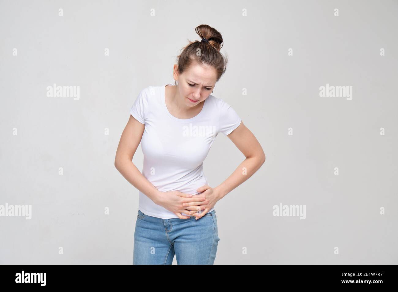 A girl in a white Tshirt and jeans is massaging her left side of the