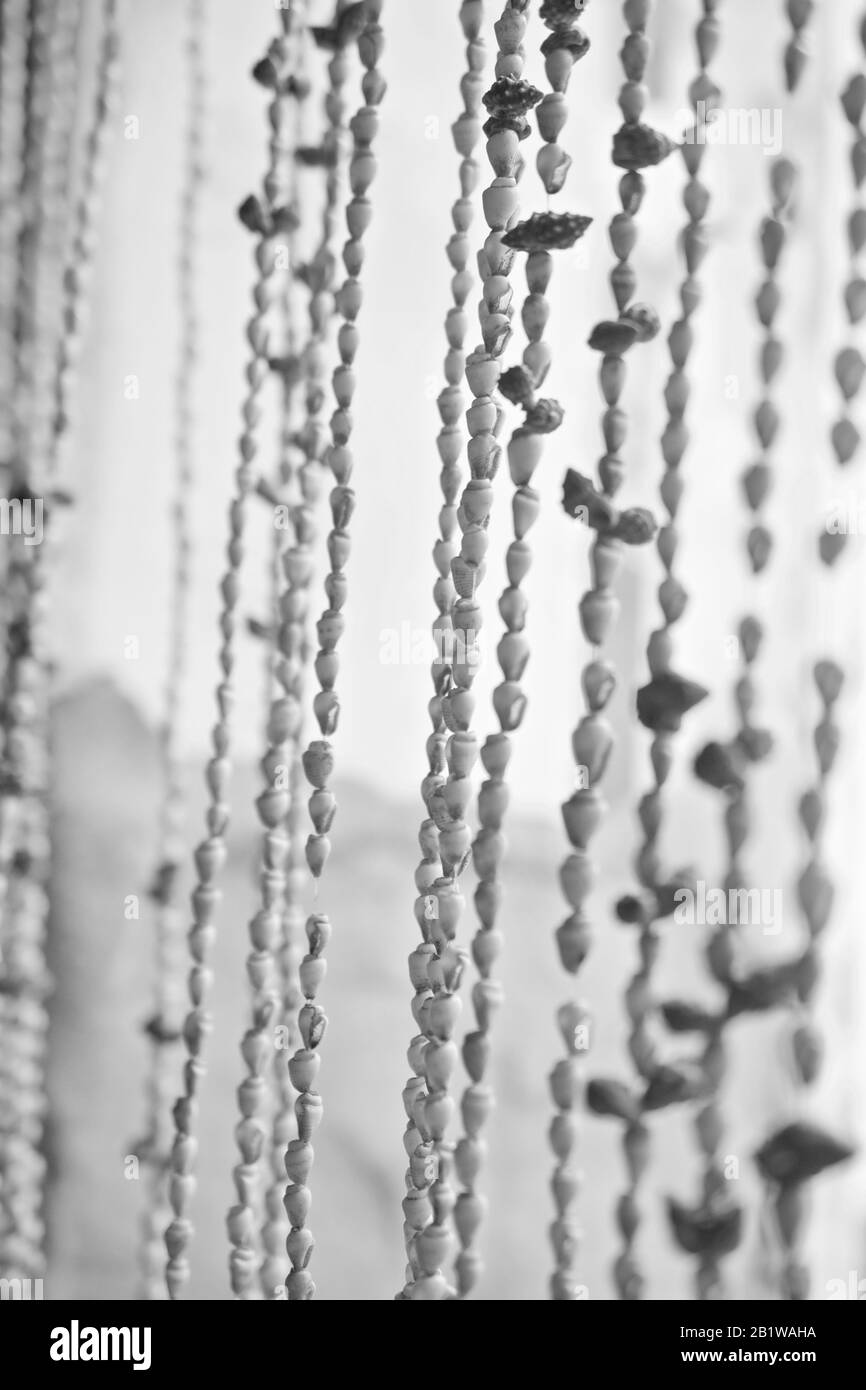 Curtain made of tiny sea shells, swaying in the wind. Select focus and motion blur. Blurry dreamy hazy. Black and white photograph. Shallow DOF. Stock Photo