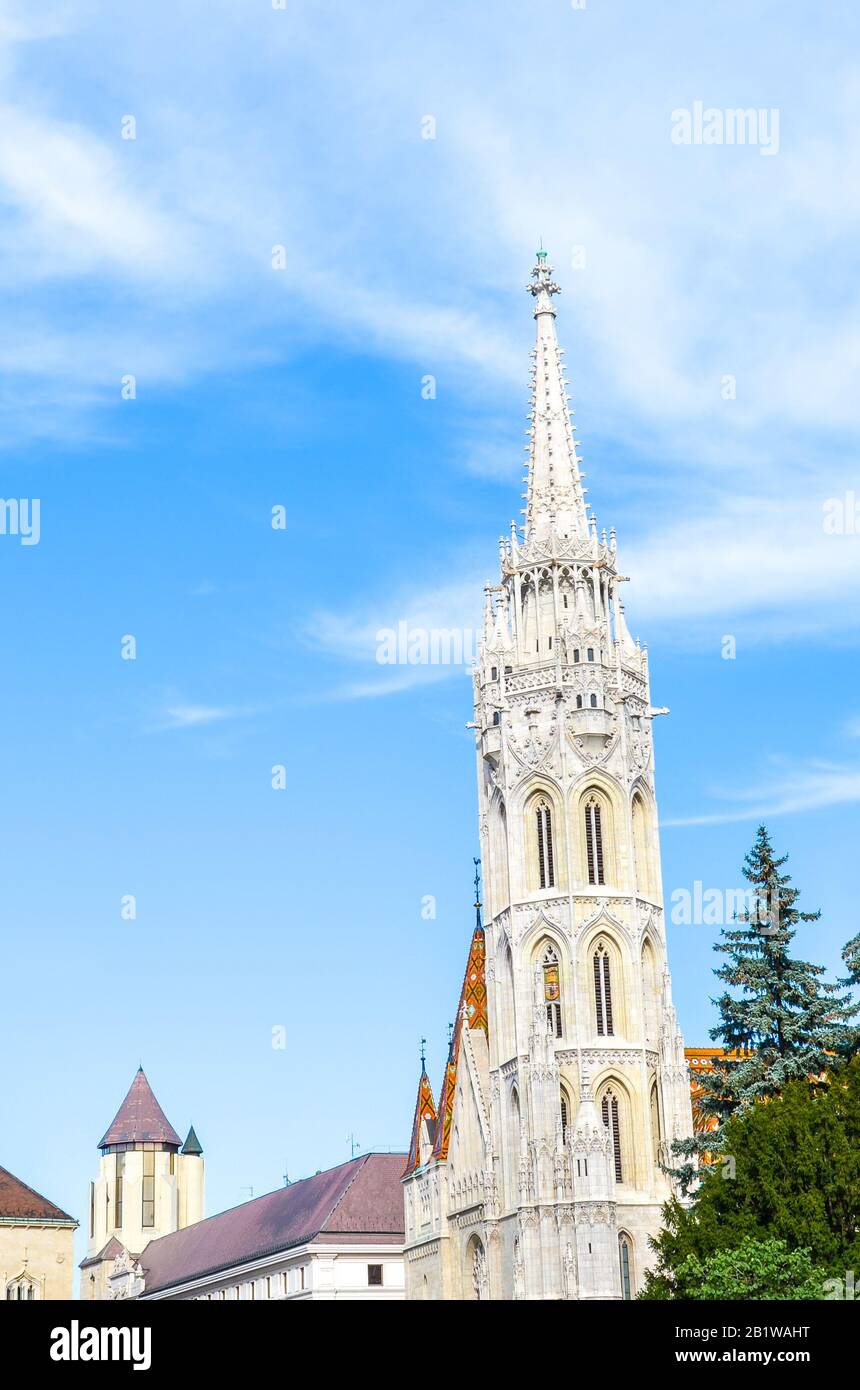 Spire of the Matthias Church in Budapest, Hungary on a vertical photo. Roman Catholic church built in the Gothic style. Blue sky and white clouds. Stock Photo