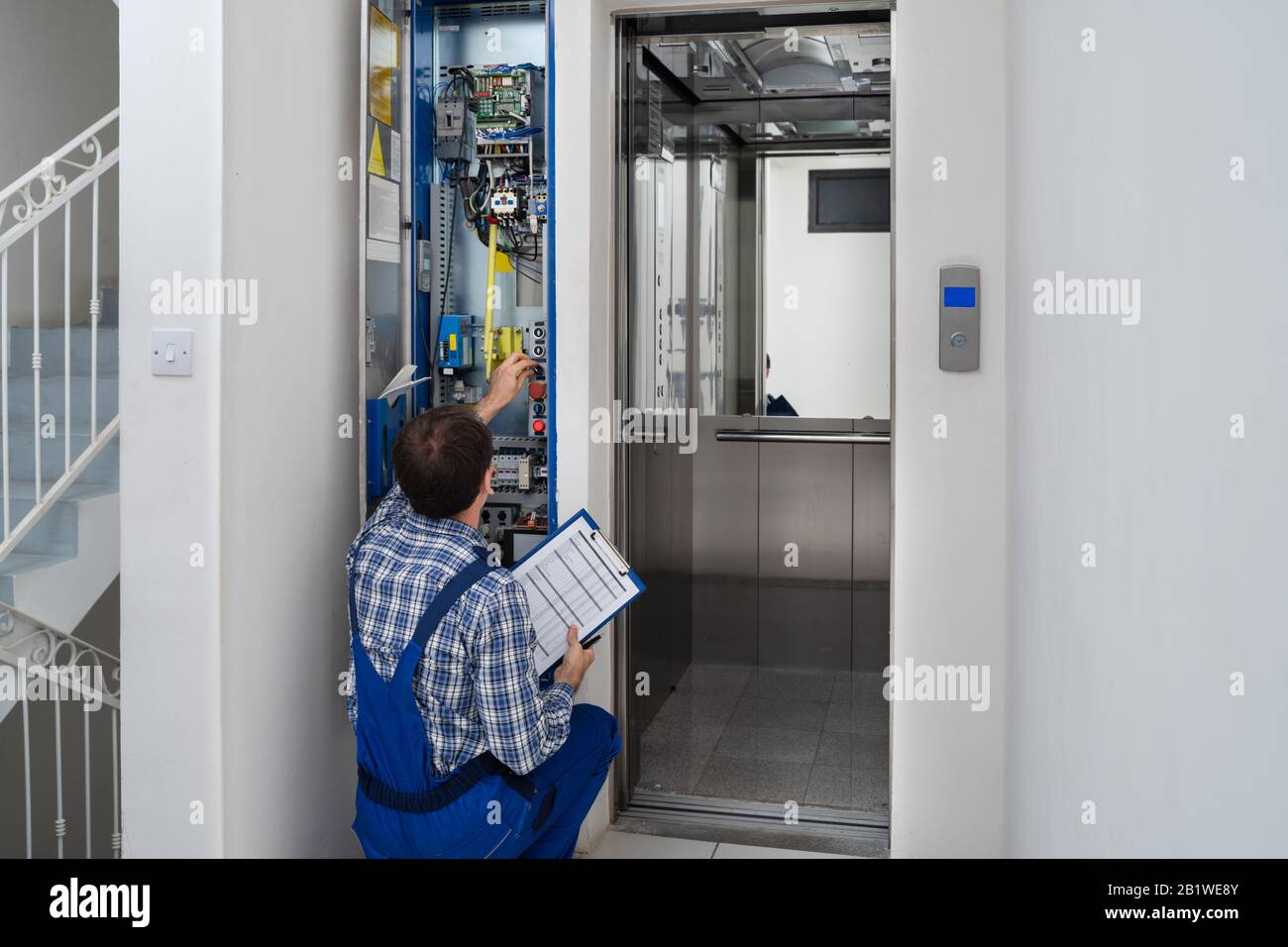 Technician Repairing Control Panel Of Broken Elevator Stock Photo