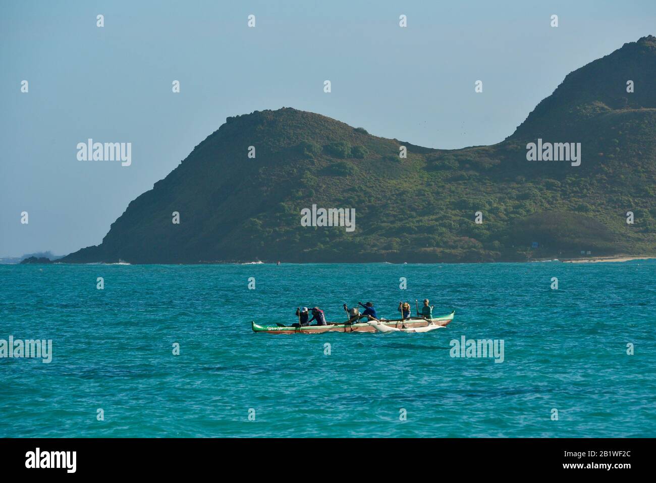 People paddling in outrigger canoe in turquoise waters off Lanikai Beach, Moku Nui island behind (part of Mokulua Islands), Oahu, Kailua, Hawaii, USA Stock Photo