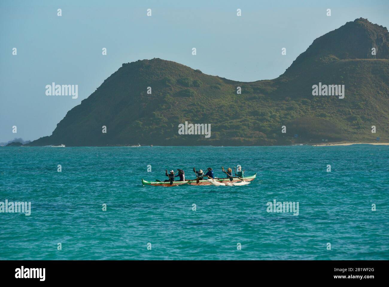 People paddling in outrigger canoe in turquoise waters off Lanikai Beach, Moku Nui island behind (part of Mokulua Islands), Oahu, Kailua, Hawaii, USA Stock Photo