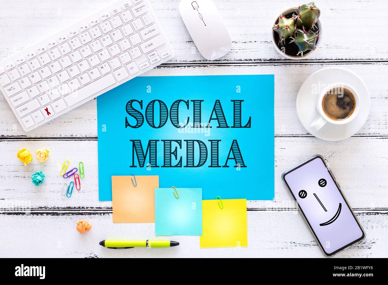 Blue card with the words "Social Media" Smaller cards with space for text, office accessories, cup of coffee, telephone, flower. White wooden backgrou Stock Photo