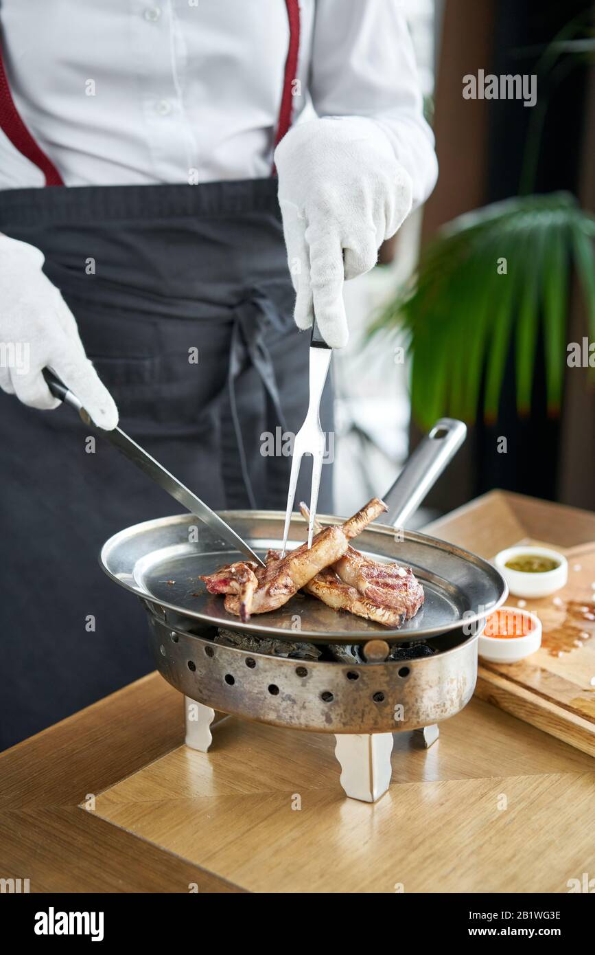 The waiter is butchering with a knife. Rack of lamb , grilled meat with