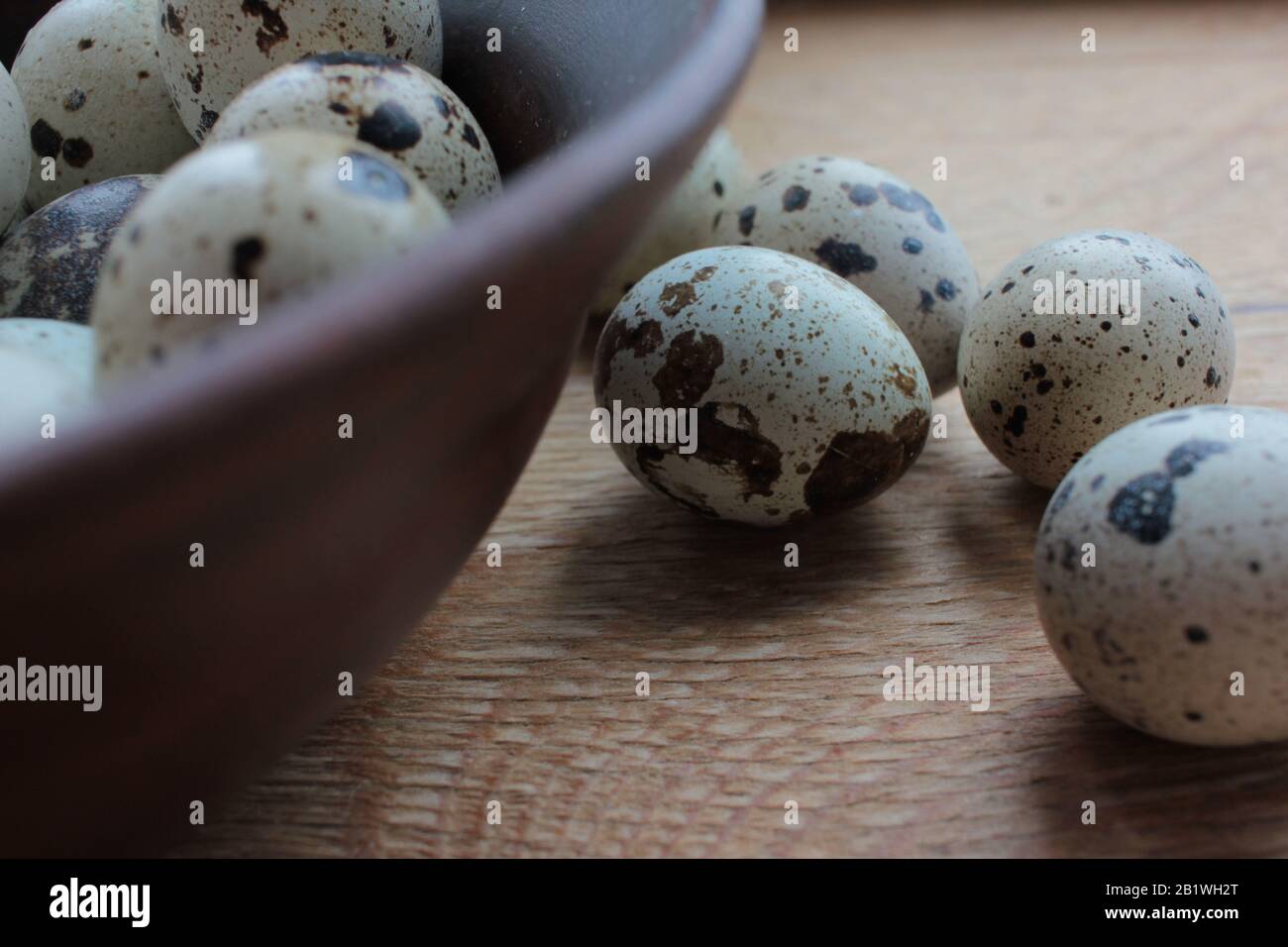 Closeup of quail eggs in brown ceramic bowl on wooden table Stock Photo