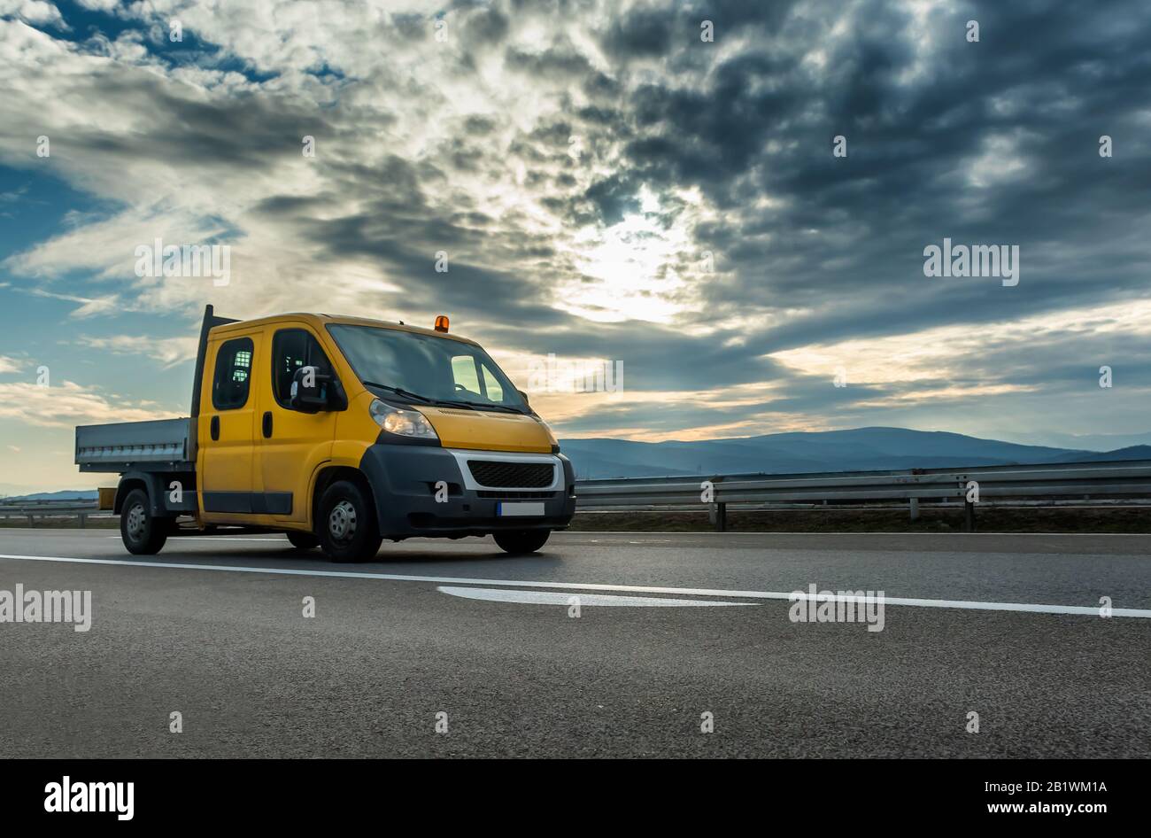 Yellow Mini Truck - Utility transportation van or mini truck driving through highway with dramatic sunset sky in the background. Transportation vehicl Stock Photo