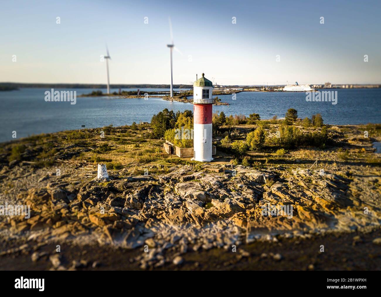 Aerial photo of beautiful white red striped sea beacon on stone island with two windmills behind, safe navigation and sea transport in baltic sea Stock Photo
