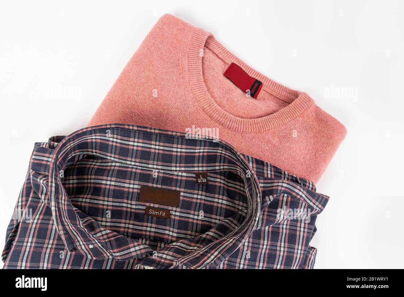 a pink wool sweater and a checkered shirt on a white surface Stock Photo
