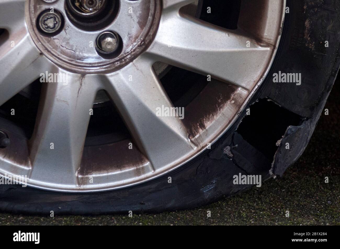 A large hole in the wall of a tyre after a blowout.  The rim of the alloy wheel is also damaged. Stock Photo