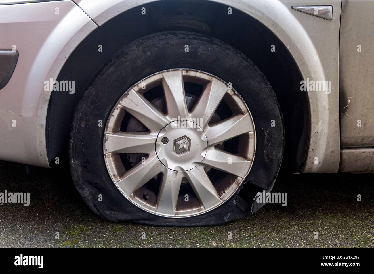 A large hole in the wall of a tyre after a blowout.  The rim of the alloy wheel is also damaged. Stock Photo