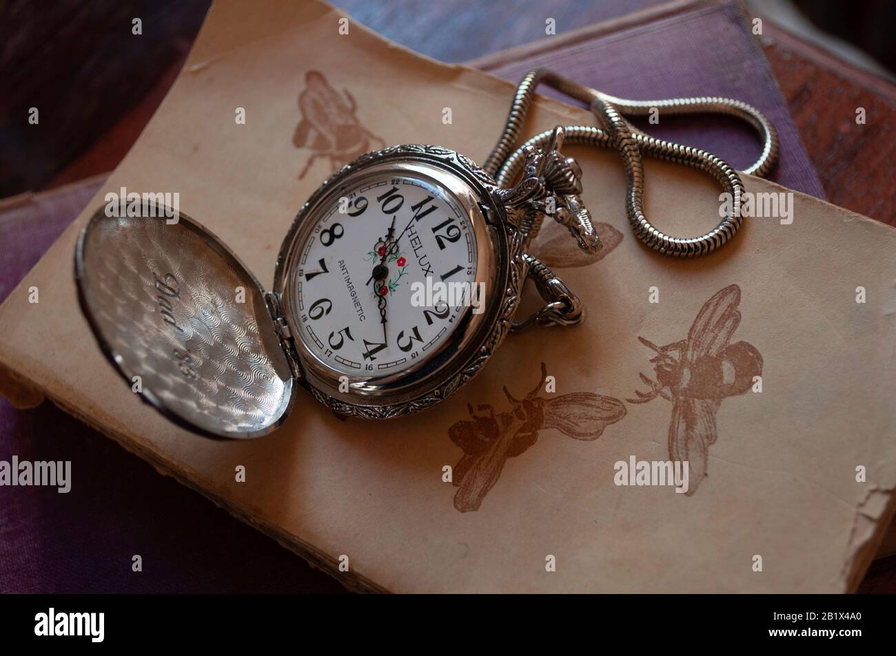 Silver pocket watch engraved with 'Dad '83' on old books Stock Photo